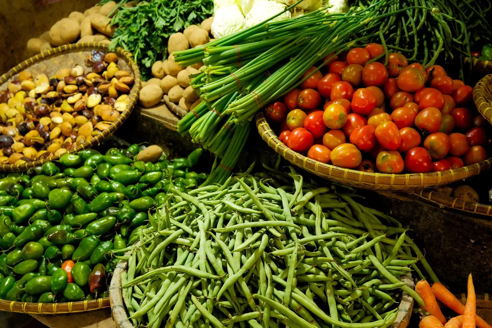 Baskets of fresh tomatoes, green beans, peppers, spring onions and potatoes at a market